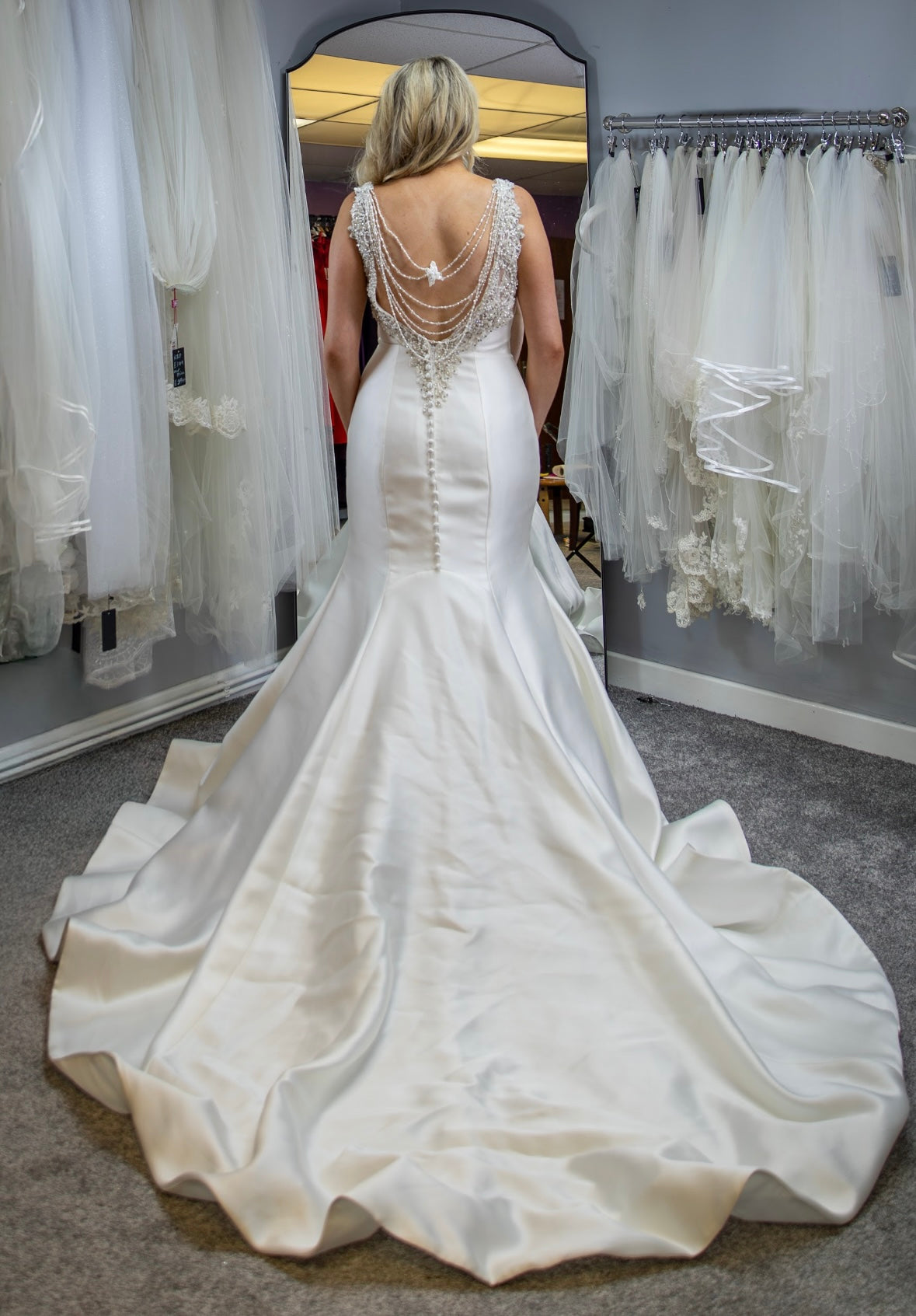Woman trying on a white wedding dress in a fitting room.